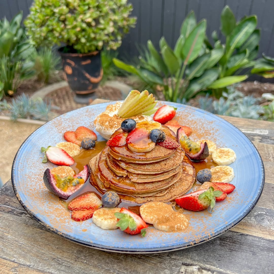 Stack of pancakes with berries and passionfruit in the garden courtyard