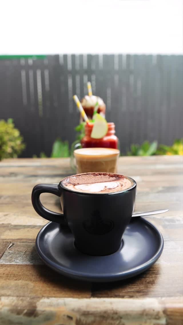 Barista-made mocha in a black cup on a timber table at Alimento